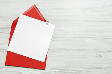 Envelope with blank paper card on white wooden table, flat lay. Space for text