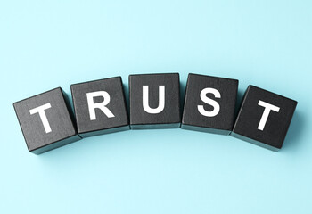 Obraz premium Word Trust made of black cubes on light blue background, flat lay