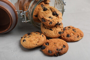 Overturned glass jar with delicious chocolate chip cookies on light grey table, closeup