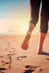 legs of woman walking on sand of beach marking her footprints as she walks away