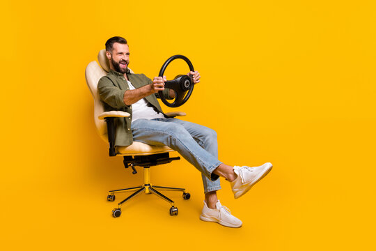 Full body profile side photo of young guy have fun play videogame steering wheel sit stool isolated over yellow color background