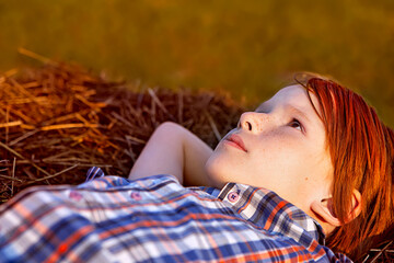 A boy with red hair and freckles lies on the hay and looks up dreamily