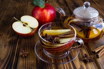 Tea with apple, cinnamon and anise in the glass cup and teapot on the wooden  background. Closeup.