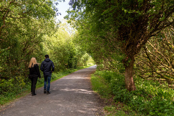 Couple walking in a forest park on a small foot path. Back to camera. Romantic time on open air. Spending time together.