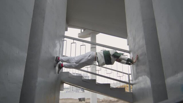 Low angle shot of parkour athlete climbing between two concrete walls while working out outdoors at urban staircase