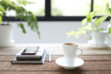 Ceramic white coffee cup and notebook and phone with plant pot on wooden table