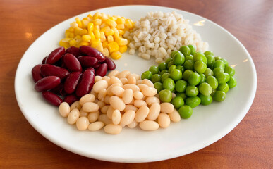 top view of navy bean and red bean and corn and  green peas and millet in white plate on wood background