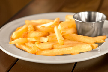 French fries on a plate with ketchup.
French fries are served on a tray with or without sauce. On a wooden table.