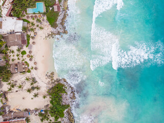 Top down aerial view of white sand beach by the blue and wavy Caribbean Sea on a cloudy morning in Tulum 