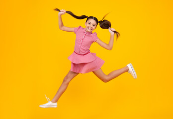 Happy teenager, positive and smiling emotions of teen girl. Excited teenager. Full length funny teenager kid jump enjoy rejoice win isolated on yellow background. Small child girl in dress jumping.