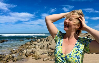 an adult woman of 35-45 years old, great joy is expressed opened her mouth and is happy from behind, in the background, she has a sea or ocean and large stones, place for a text about travel.