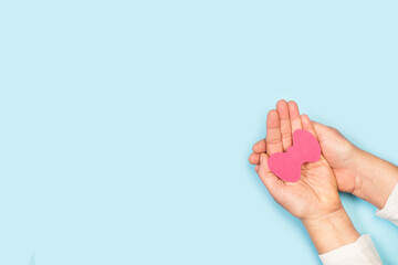 Manos de mujer sosteniendo glándula de tiroides en papel rosa sobre un fondo celeste liso y aislado. Vista superior y de cerca. Copy space. Concepto:  Día Mundial de la Tiroides.  - obrazy, fototapety, plakaty