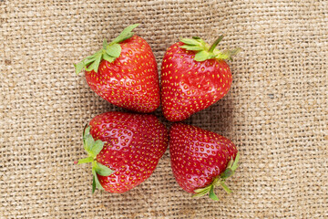 Several berries of ripe organic strawberries on jute fabric, close-up, top view.