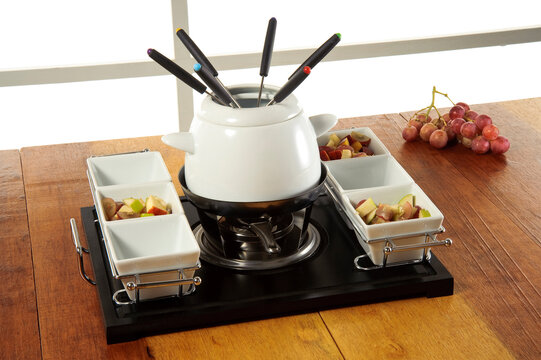 White ceramic fondue set with a rechaud and six forks, ambiented, with fruit pots