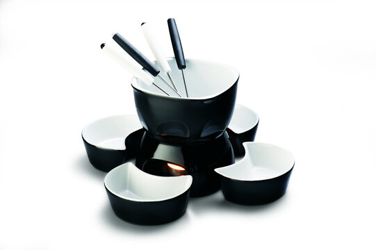 Black and white ceramic fondue set with rechaud, four forks and pots, isolated