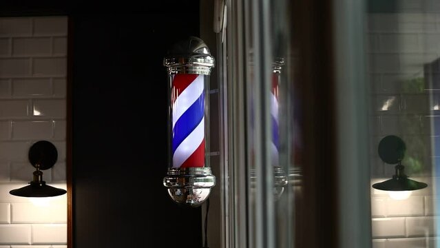 Barber pole spinning at night. International barbershop pole sign. A barber pole calling for people at street. Vintage barbershop. Salon