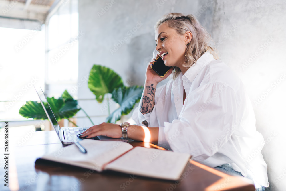 Aufkleber millennial blonde woman using netbook technology for browsing booking information while calling via 