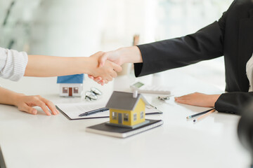 A saleswoman checks the lease and holds a small gray model of house and house keys in preparation for meeting customers to sign the lease. Real estate leasing concept.