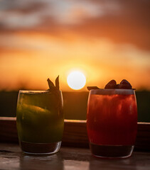 Red and green cocktails on a wooden table with sunset background