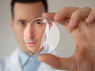 Eye care professional optometrist doctor man holding a glass lens inside laboratory - obrazy, fototapety, plakaty