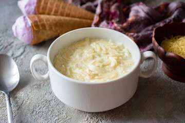 A hearty lunch for the whole family: milk soup with vermicelli in a white plate on a gray background. Close-up