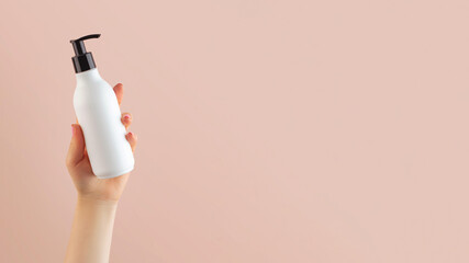 A mockup of a white dispenser with a cosmetic product in a woman's hand on a light pink background.