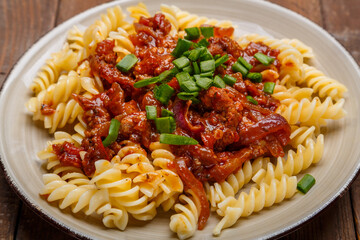 Beige plate with bolognese pasta on a wooden table sprinkled with green onions close-up.