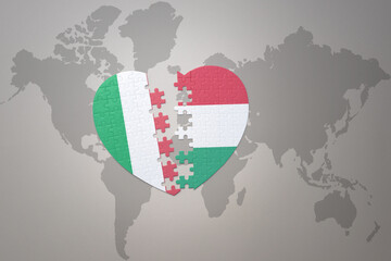puzzle heart with the national flag of hungary and italy on a world map background. Concept.