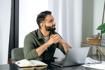 Thoughtful Indian or Arabian successful man in casual wear, broker, manager, sits at a desk in the...