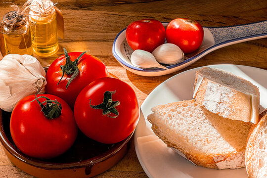 Receta t&iacute;pica Catalu&ntilde;a. Pan con tomate untado y aceite sobre encimera de madera y un bol con ajos. 