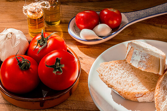 Receta t&iacute;pica Catalu&ntilde;a. Pan con tomate untado y aceite sobre encimera de madera y un bol con ajos. 