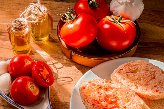 Receta t&iacute;pica Catalu&ntilde;a. Pan con tomate untado y aceite sobre encimera de madera y un bol con ajos. 