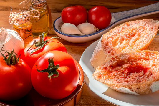 Receta t&iacute;pica Catalu&ntilde;a. Pan con tomate untado y aceite sobre encimera de madera y un bol con ajos. 
