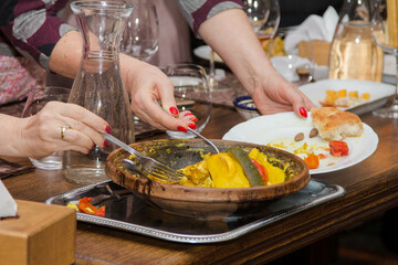 Hands with forks take food from a dish of stewed vegetables in a restaurant
