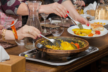 Hands with forks take food from a dish of stewed vegetables in a restaurant