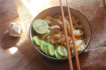 Pork Fried Rice, Chinese Style Fried Rice in a Bowl with Cucumber and Lemon Served on a brown wooden table.