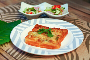 Fried bread with minced pork spread with cucumber dipping sauce on a wooden table.