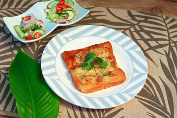 Fried bread with minced pork spread with cucumber dipping sauce on a wooden table.