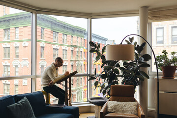 Man sits working on his digital tablet at a desk in the window with the city behind him