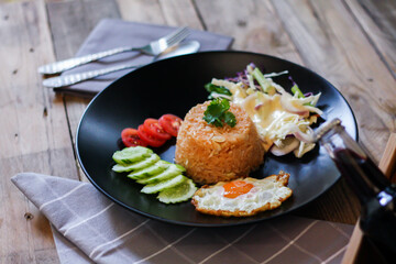 Fried rice, fried egg, cucumber, sliced tomato, green salad and Fried chicken placed on a black plate as a garnish.