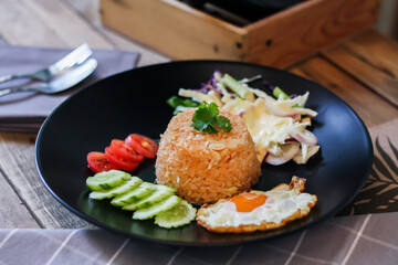 Fried rice, fried egg, cucumber, sliced tomato, green salad and Fried chicken placed on a black plate as a garnish.