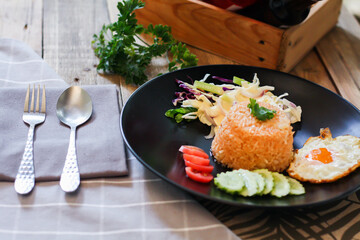 Fried rice, fried egg, cucumber, sliced tomato, green salad and Fried chicken placed on a black plate as a garnish.