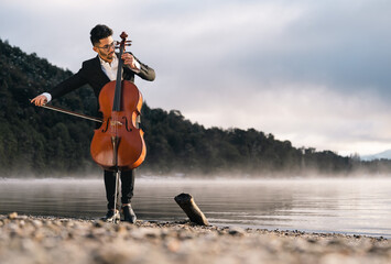 Musician playing cello by the lake on a misty morning