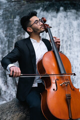 musician playing cello by a waterfall wearing glasses