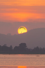 Paraglider flying aligned with the sun as it sets behind the mountain at sunset on the coast of Cantabria, Spain.