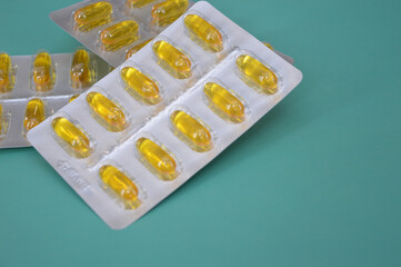 Yellow Omega 3 capsules in blisters lying in a row on a green background. Fish oil, dietary supplement, drugs, medicine, prescription. Health care concept.