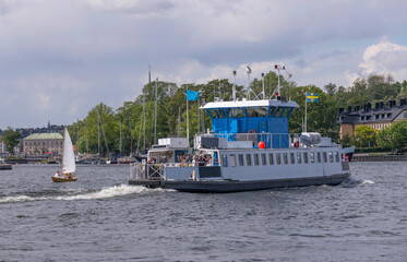 Ferry passing the bay Vasadjupet between the islands Djurg&aring;rden and Kastellholmen  a sunny summer day in Stockholm