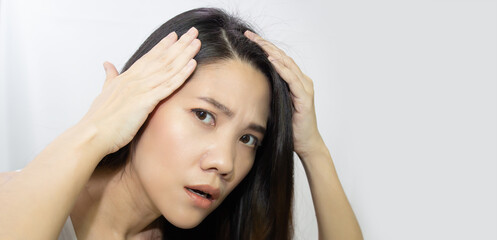 Asian Beautiful woman use hand touch her head and looking to check grey hair with a worry face.