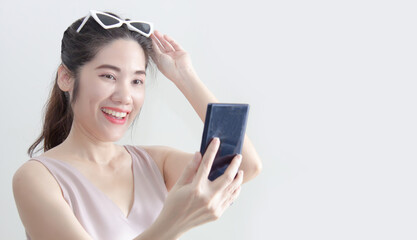 Fototapeta premium Asian beautiful woman looking on smartphone and raise hand touch on sun glasses and smile with happiness during chatting or shopping online or win a lottery or win game