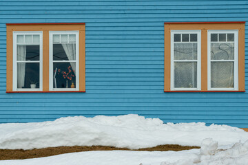 Two single hung windows with orange trim on a blue exterior wall of a vintage style building. The...